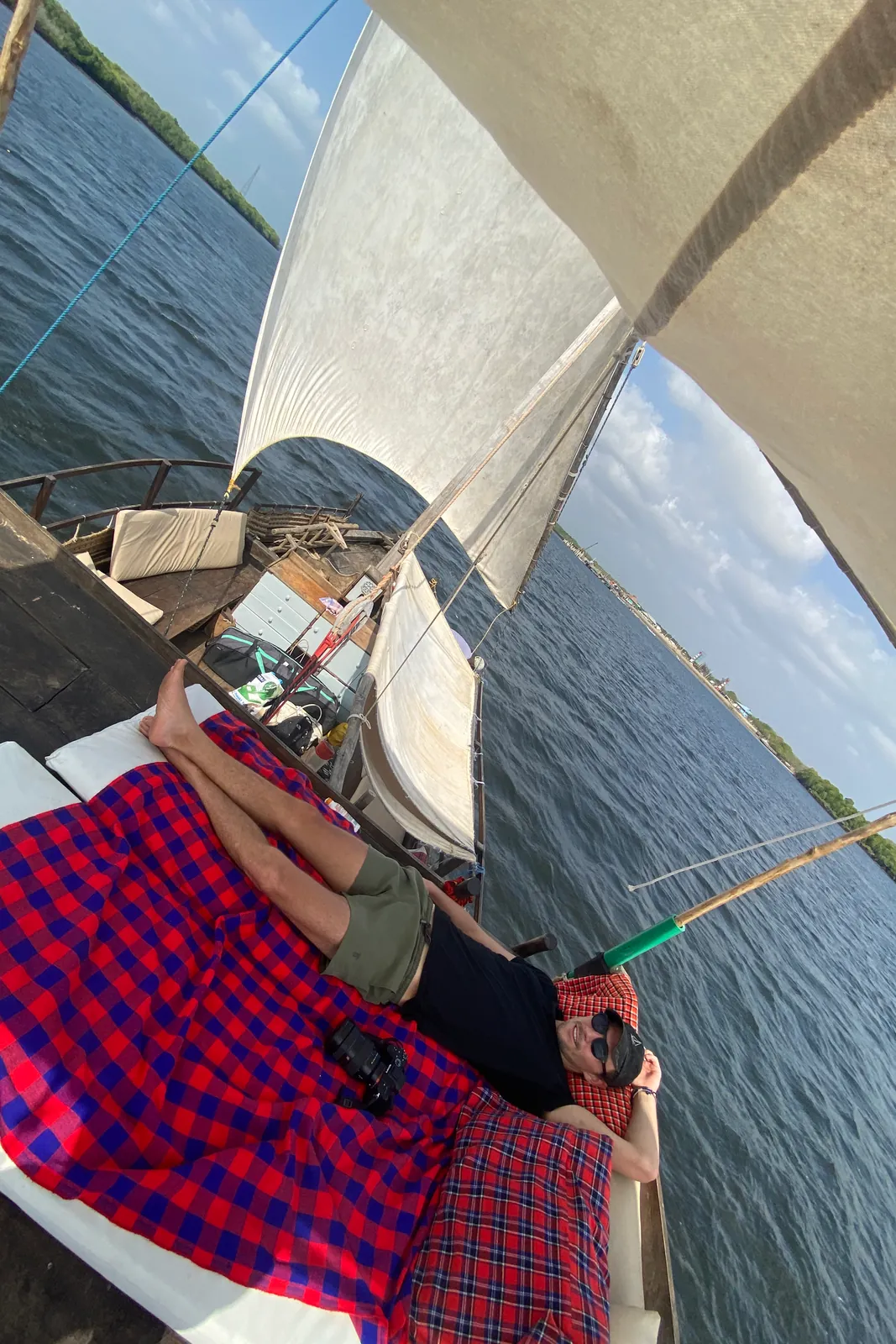 A guest stretched out on a Maasai blanket on deck beneath the sail