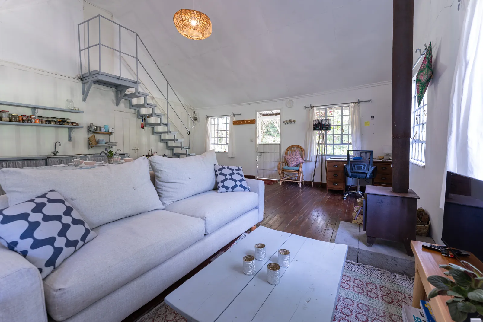 The living room at Gilgil Nest, with a white sofa and a spiral staircase to the loft
