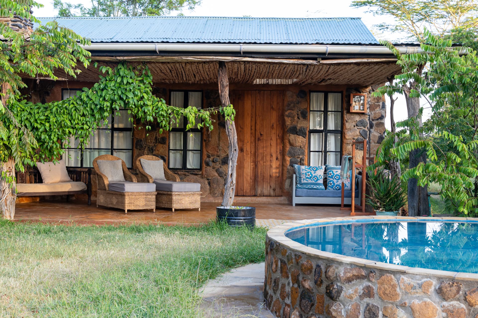 The stone verandah at Laikipia Nest with wicker chairs, shaded by a fig tree beside the round stone swimming pool