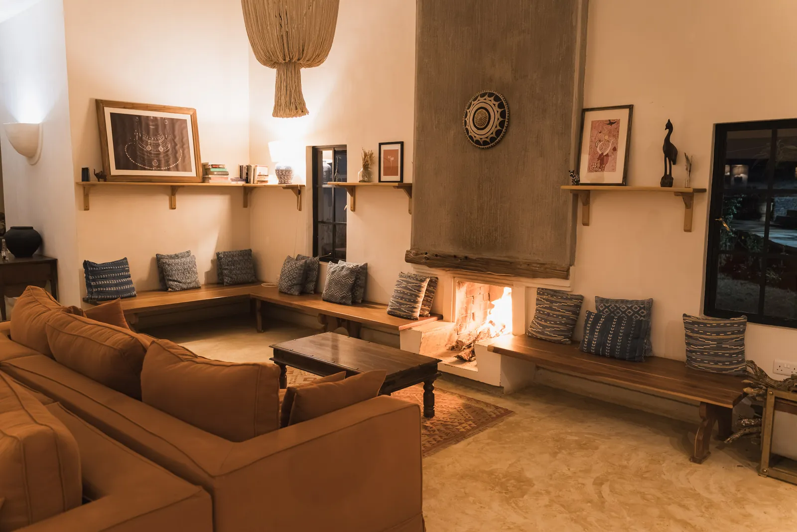 The sitting area at Lolldaiga Nest, a low rust sofa and built-in benches around a lit fireplace