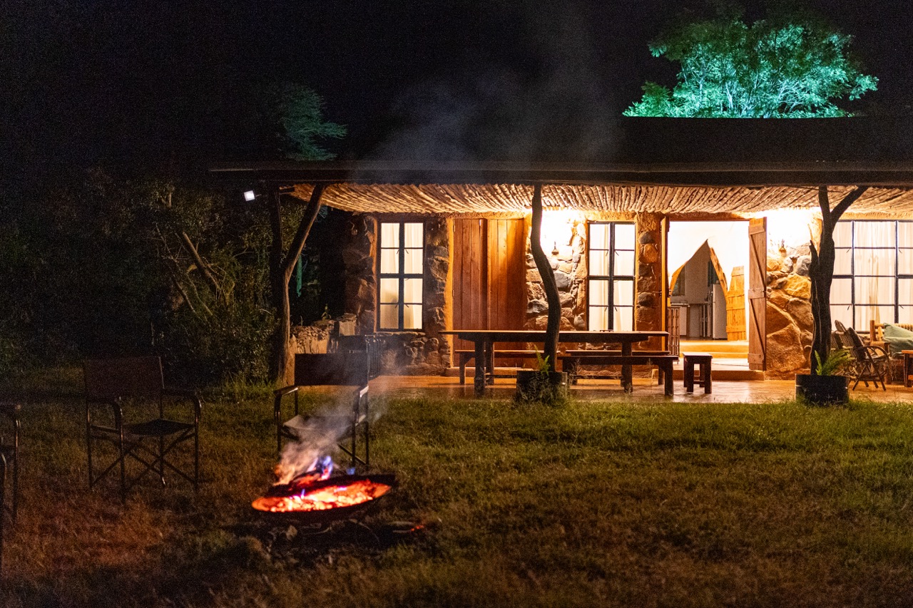 The house at Laikipia Nest lit from inside at night, with the firepit burning on the lawn