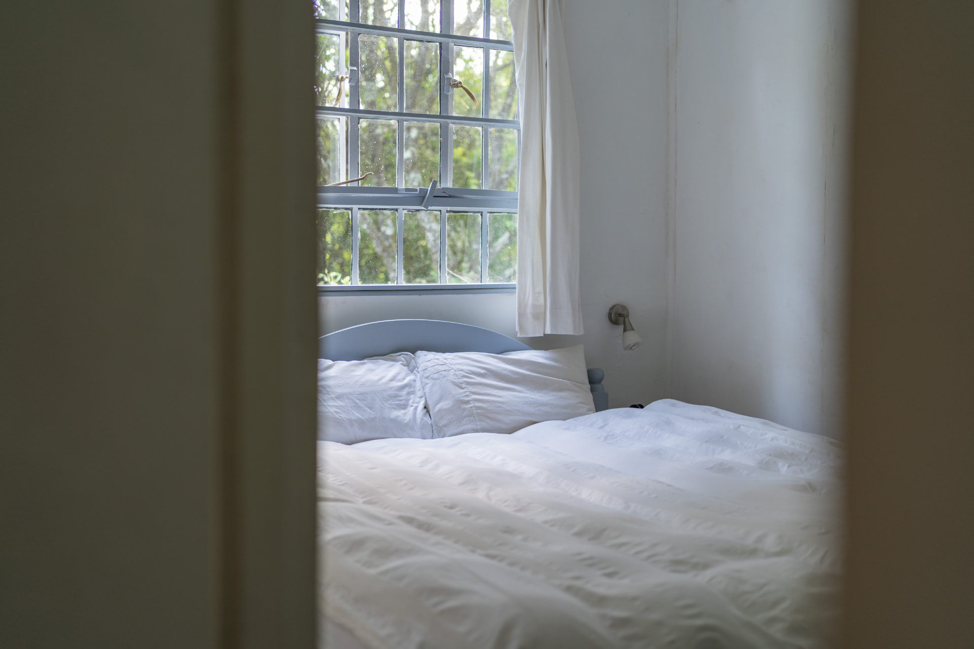 Bedroom one at Gilgil Nest, a double bed in white linen below a tall garden window