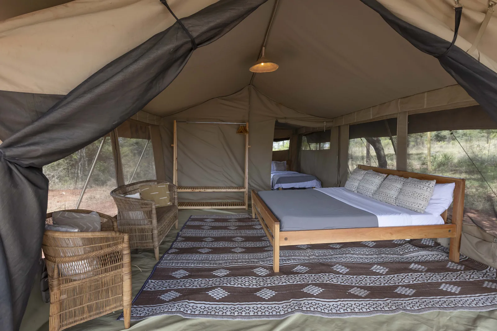 Inside the safari tent at Lolldaiga Nest, a king bed with a twin bed behind, wicker chairs and a patterned rug