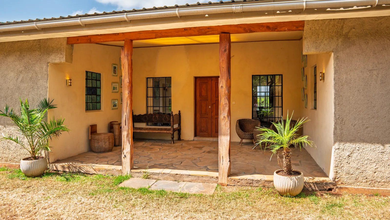 The covered verandah at Asili Cottage, with a bench and potted palms