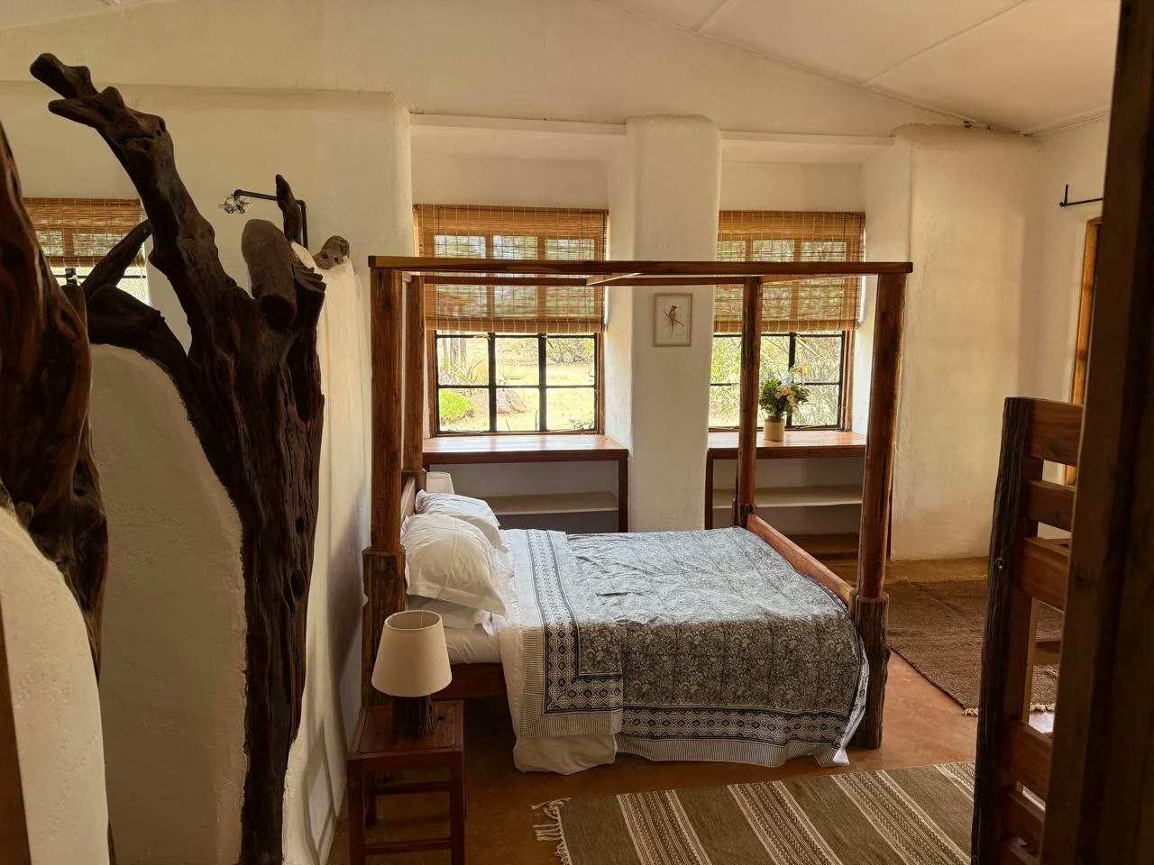 The master suite at Laikipia Nest with a wooden four poster bed and bamboo shaded windows