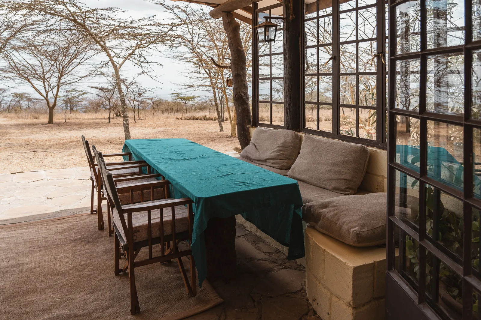 The verandah dining table at Champagne Ridge Nest, laid with a green cloth beside a cushioned stone bench, acacias beyond